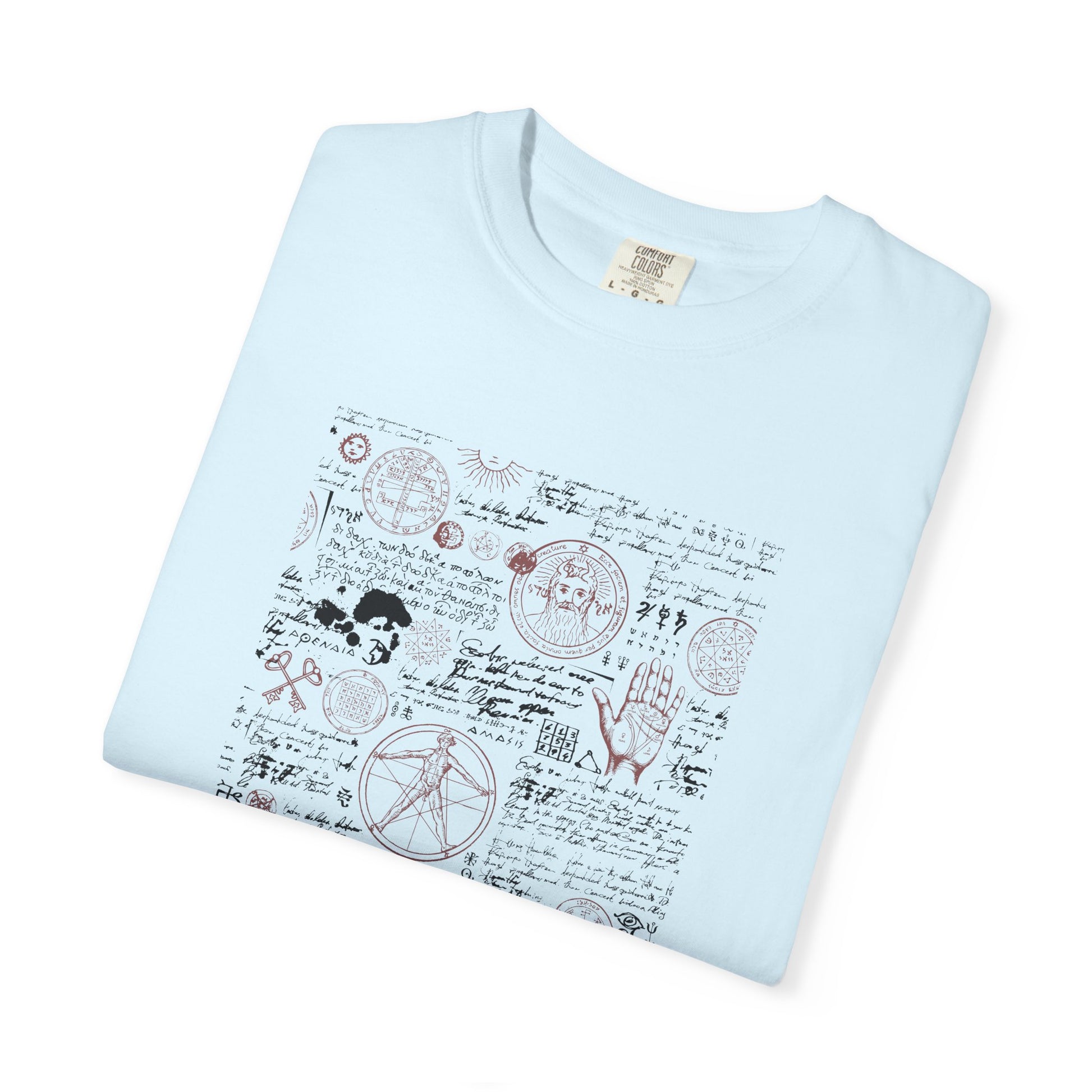 A light blue folded crewneck t-shirt featuring a detailed occult-style graphic print on the front with various symbols, handwritten script, and illustrations.