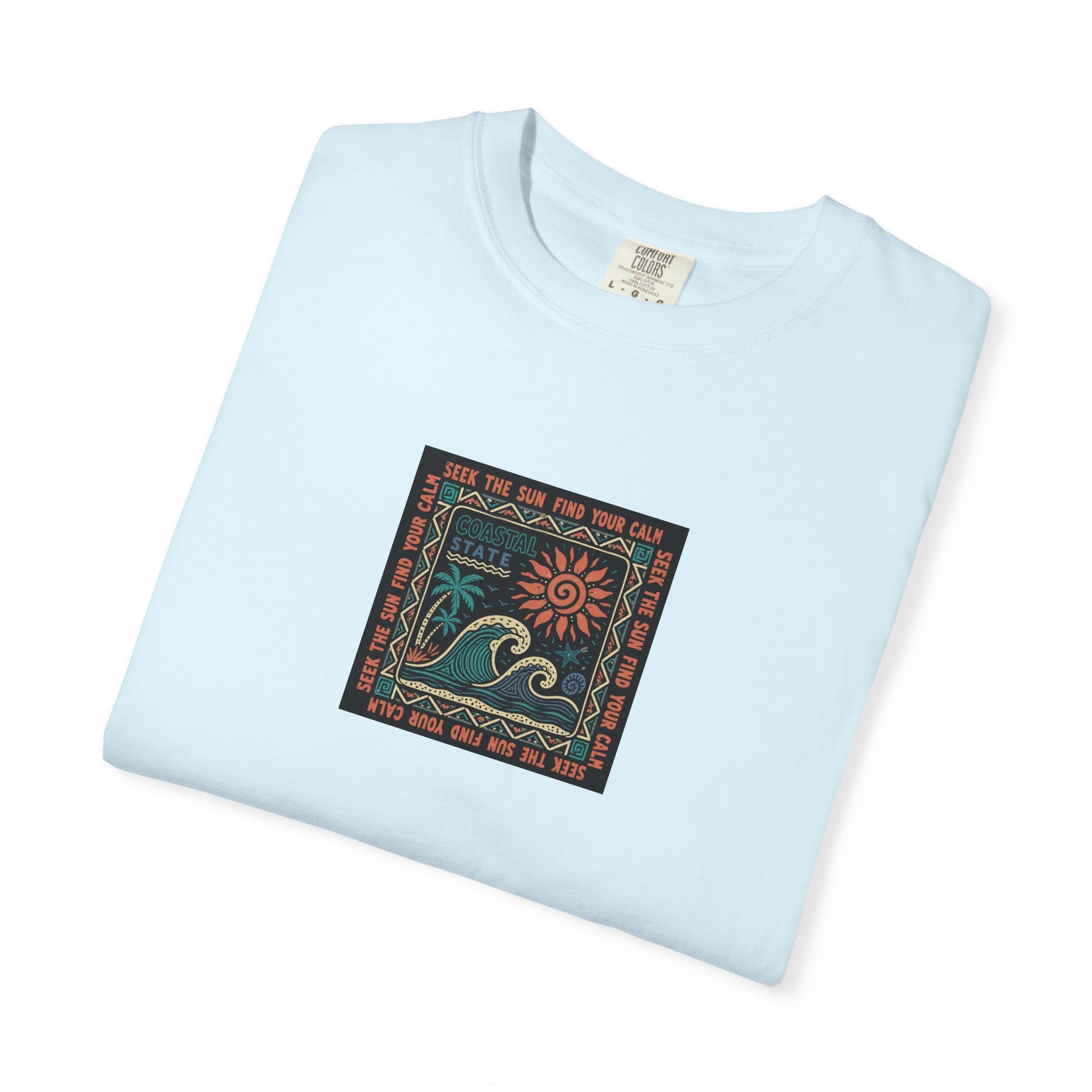 A light blue folded crewneck t-shirt with a square graphic print on the front featuring a wave, sun, and the text 'SEE THE SUN, FIND YOUR CALM'.