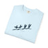 A light blue folded t-shirt with a black graphic of four surfers on a beach and the text 'Suna Tide Surfing' printed on the front, set against a plain white background.