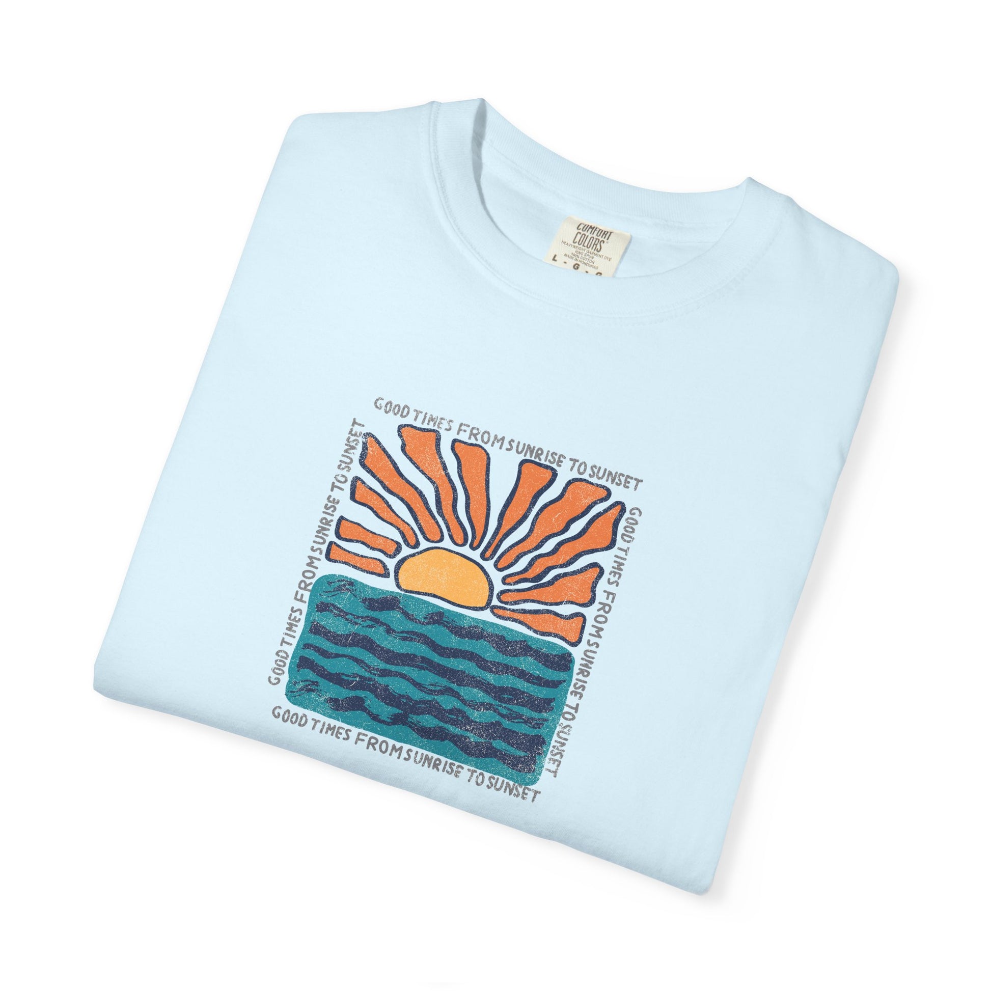 A light blue folded crewneck t-shirt with a colorful graphic print of a rising sun over wavy water and the text 'GOOD TIMES FROM SUNRISE TO SUNSET' printed around the design.