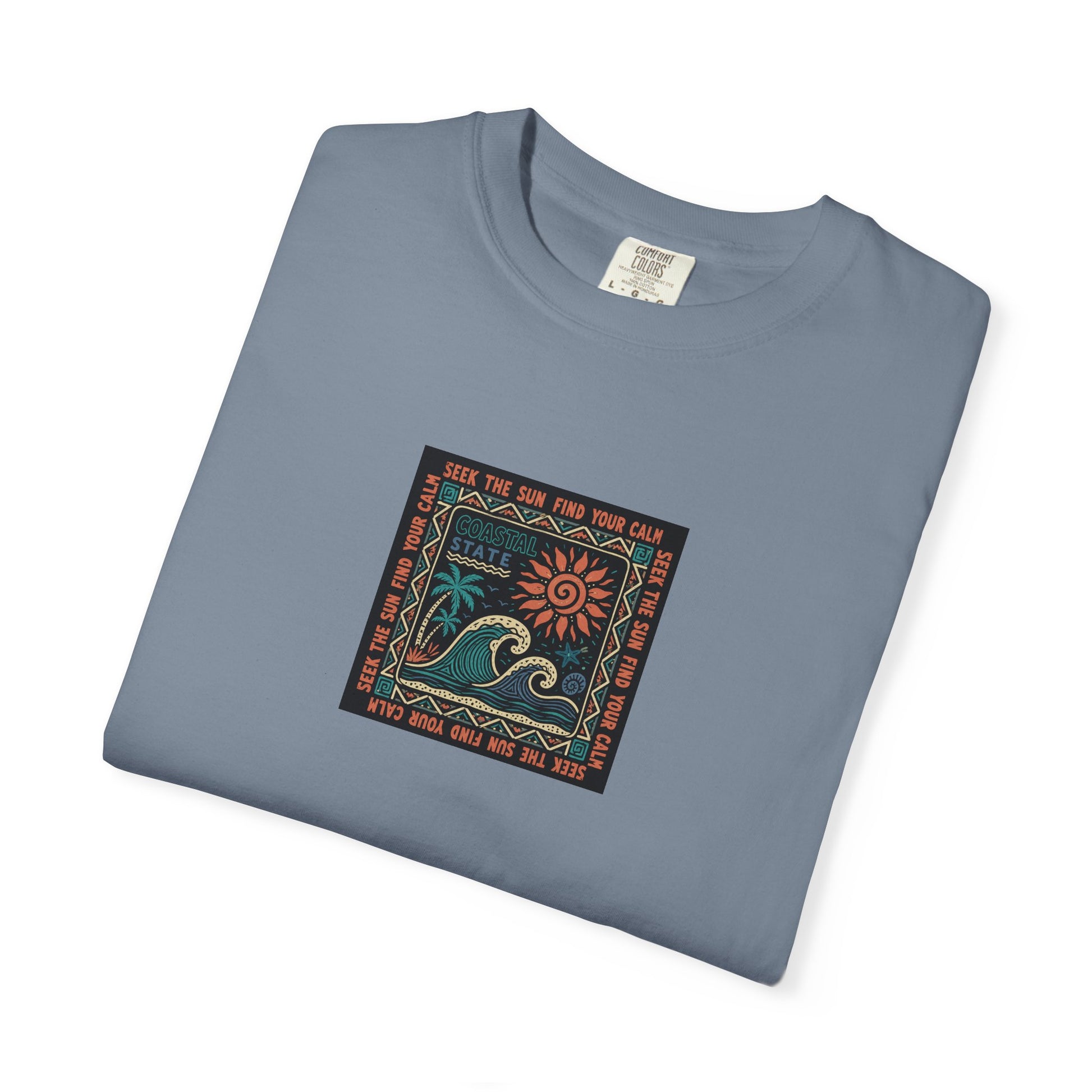 A folded slate blue t-shirt with a square graphic print on the chest featuring a wave, sun, and the text 'SEE THE SUN, FIND YOUR CALM'.