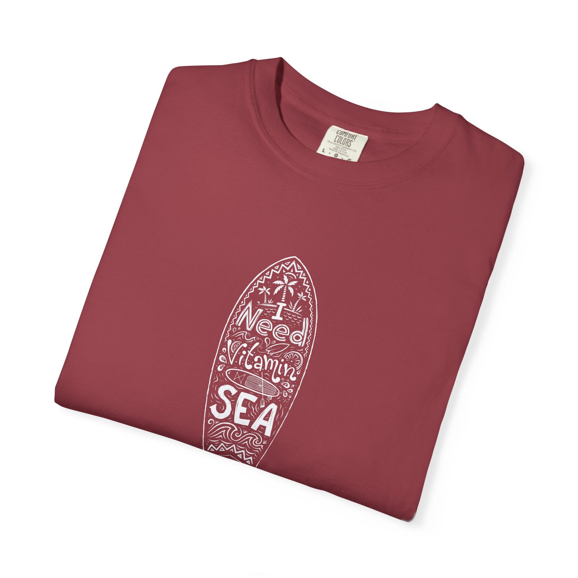 A folded dusty rose crewneck t-shirt with a white surfboard graphic containing the words 'I Weed Vitamins SEA' on a clean white background.