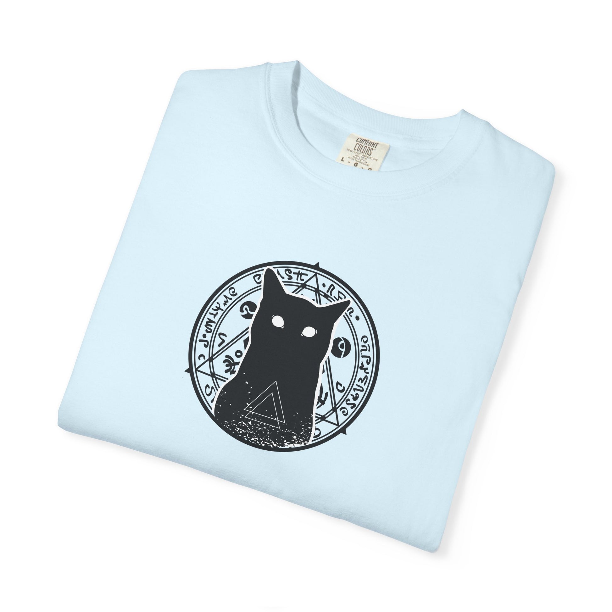 A light blue folded crewneck t-shirt featuring a black graphic of a cat inside a circular occult-style design with the word 'Wiccan' printed around it.