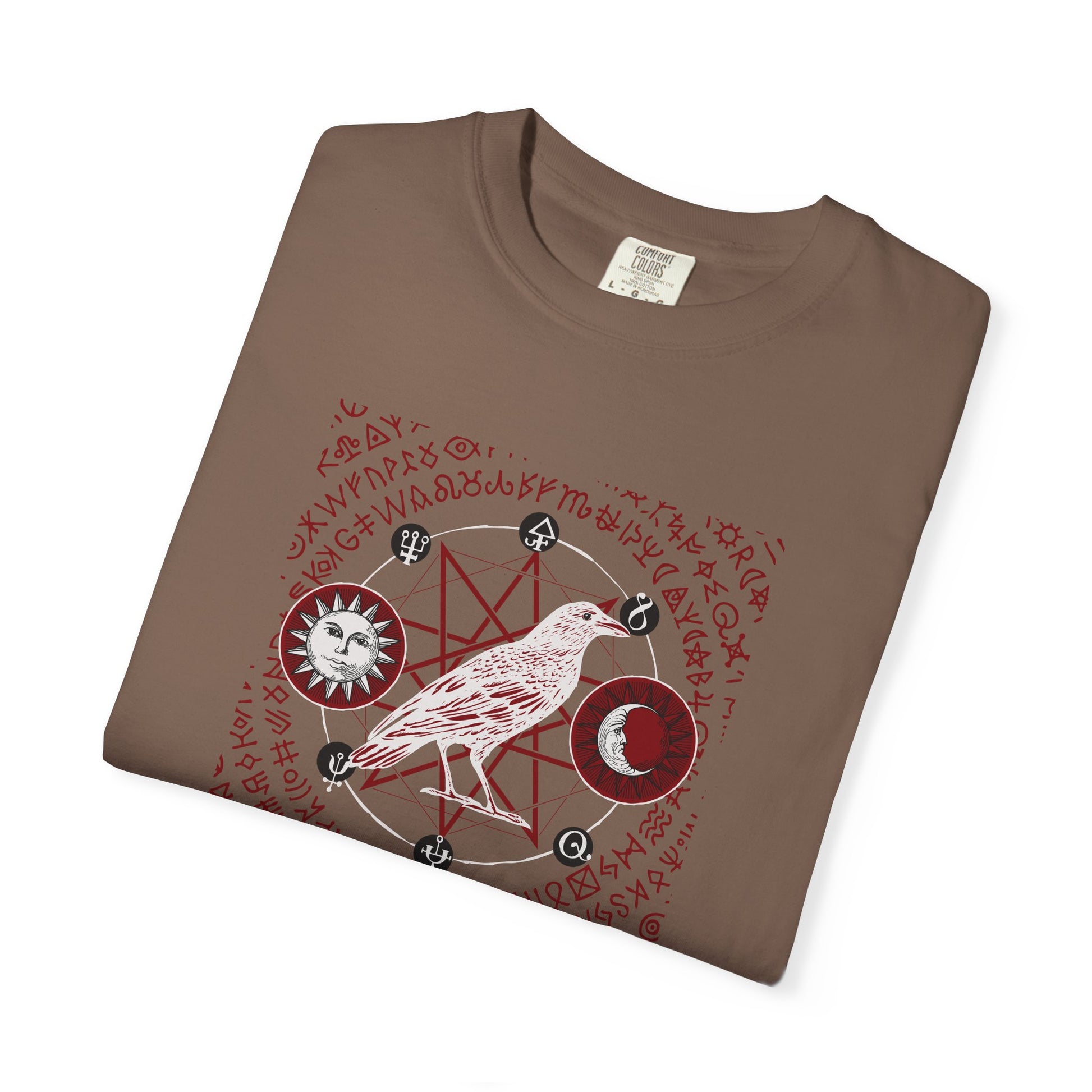 A brown folded t-shirt with a red and white occult-style graphic featuring a bird, moon, sun, and magical symbols.