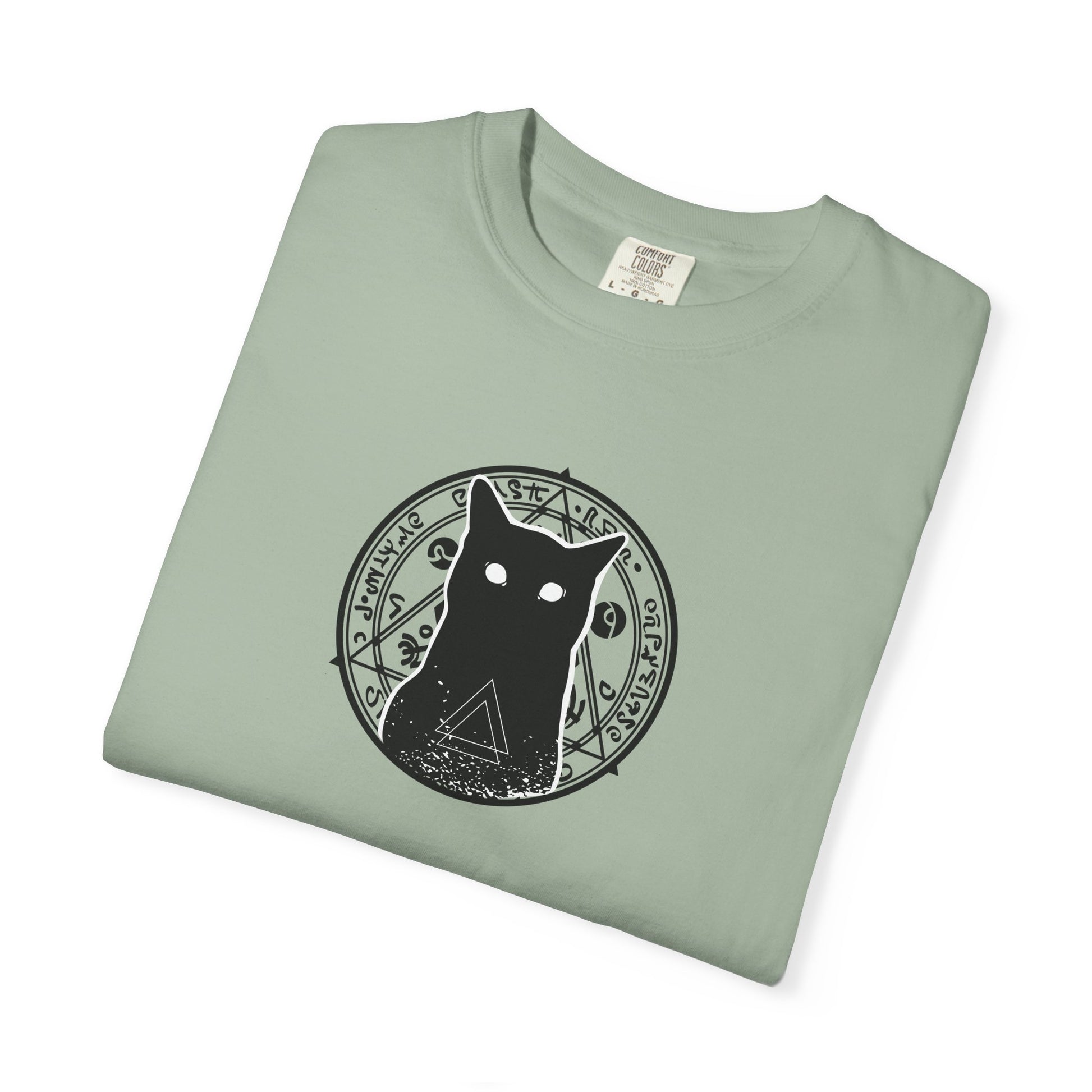 A folded sage green t-shirt with a black graphic of a cat inside a circular occult-style symbol on the chest, displayed on a clean white background.