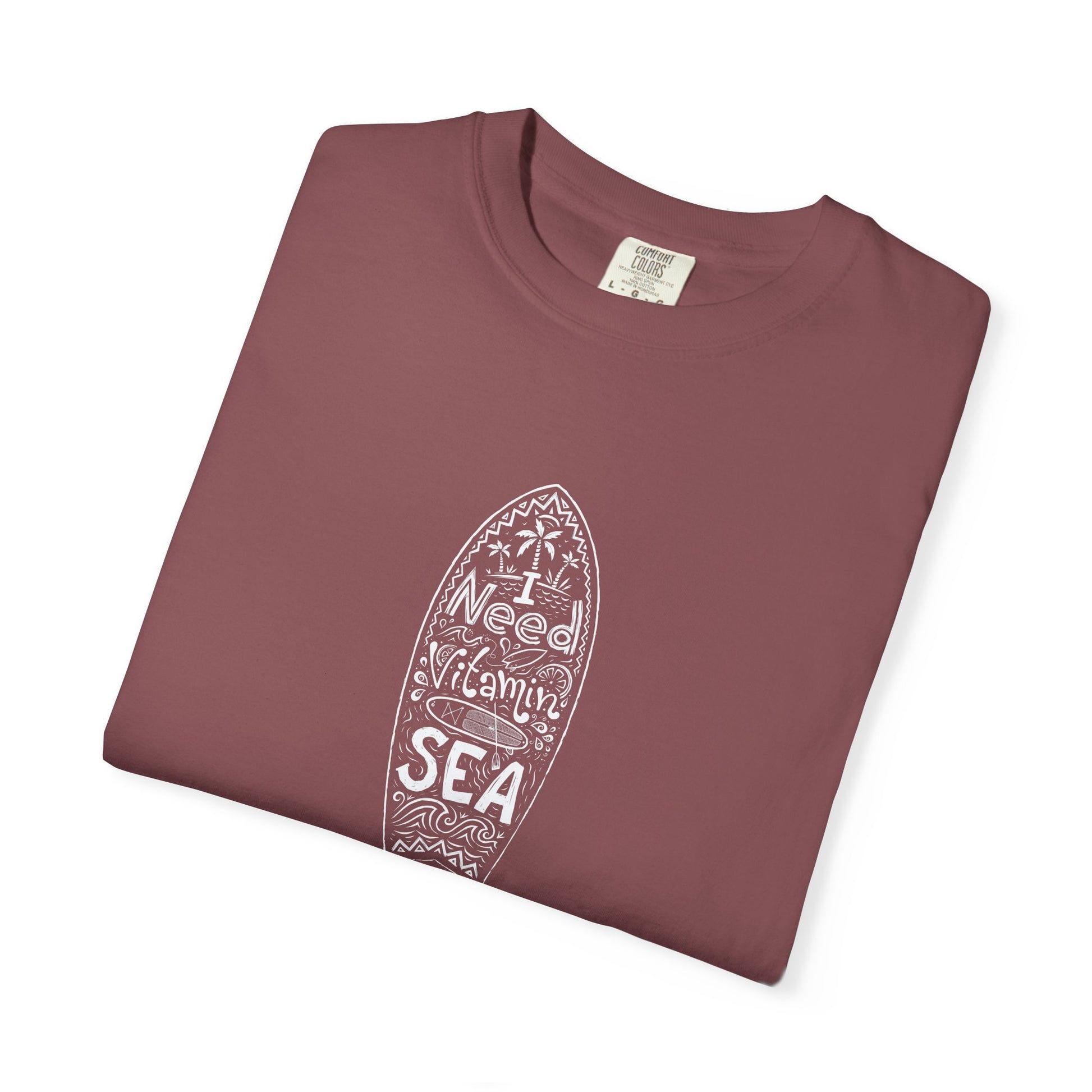 A folded dusty rose crewneck t-shirt with a white surfboard graphic containing the words 'I Weed Vitamins SEA' on a clean white background.