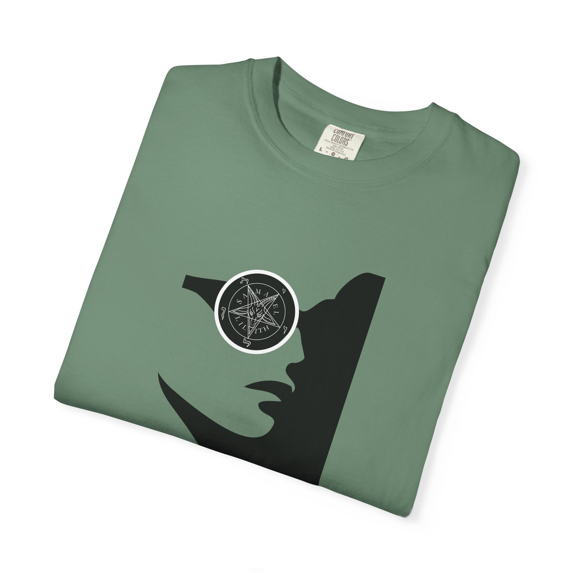 A folded sage green t-shirt with a black graphic of a woman's profile wearing a circular eyepatch with a pentagram design, shown on a white background.