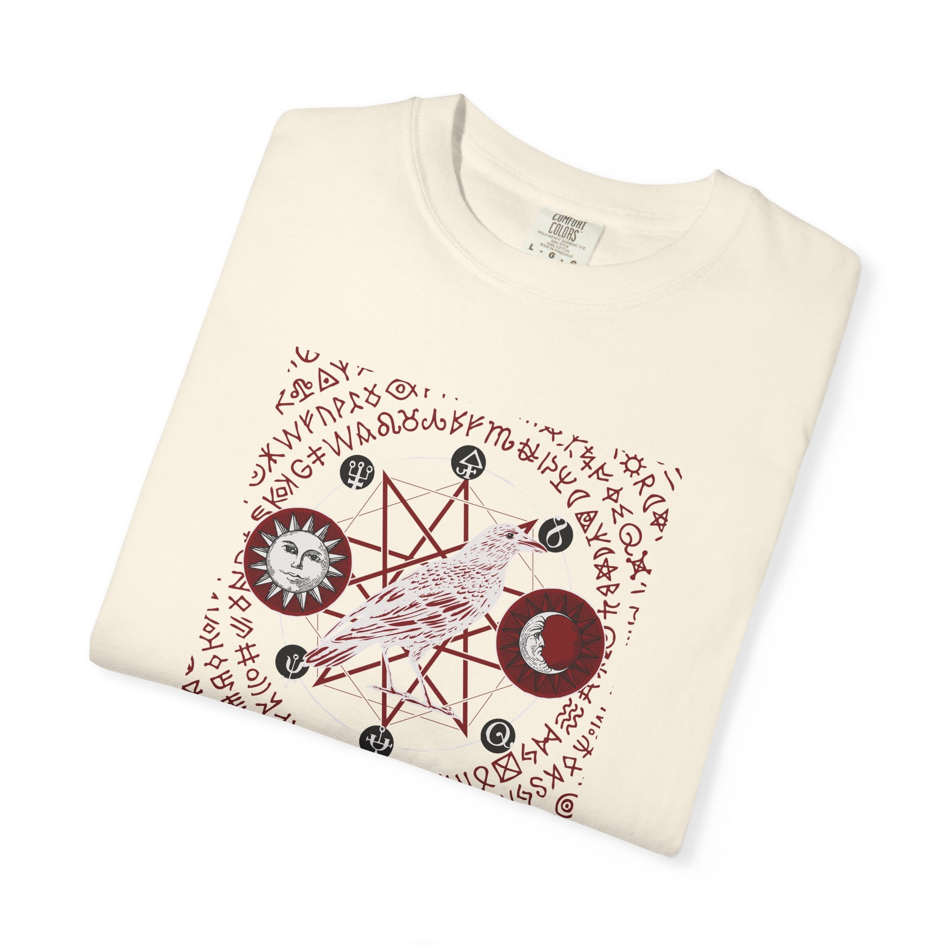 An off-white folded crewneck t-shirt featuring a detailed occult-style graphic print with a bird, moon phases, stars, and runes.